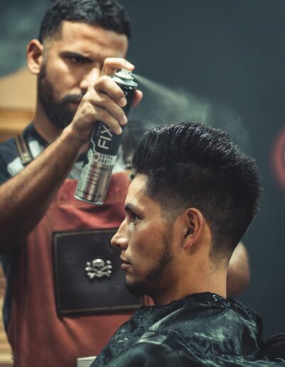 Experienced stylist applies finishing spray to client's hair during grooming session at modern barbershop.