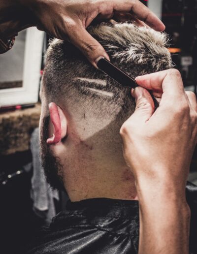 A man receives a detailed haircut with a straight razor at a barbershop, showcasing modern style.